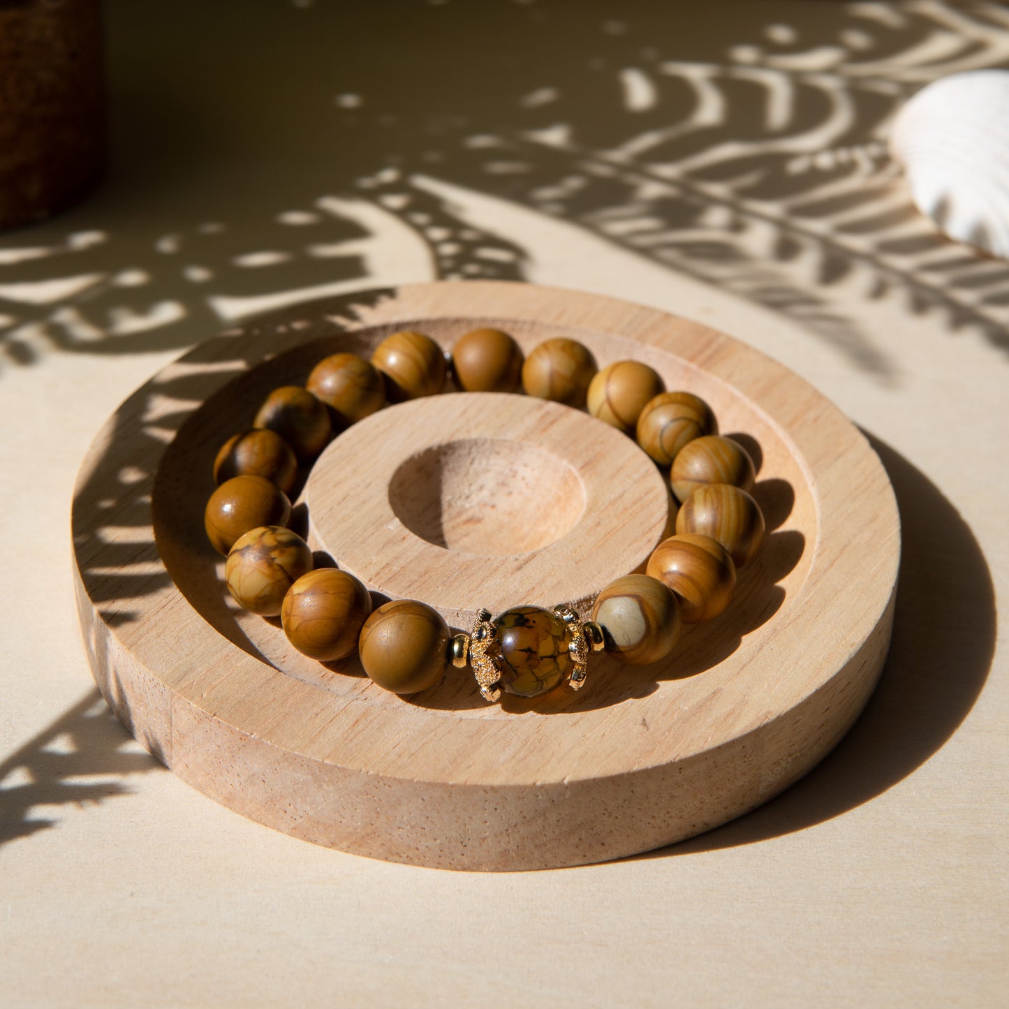 A lacewood beaded bracelet with a dragon viens agate crystal, displayed on a wooden coaster with a shell in the background.