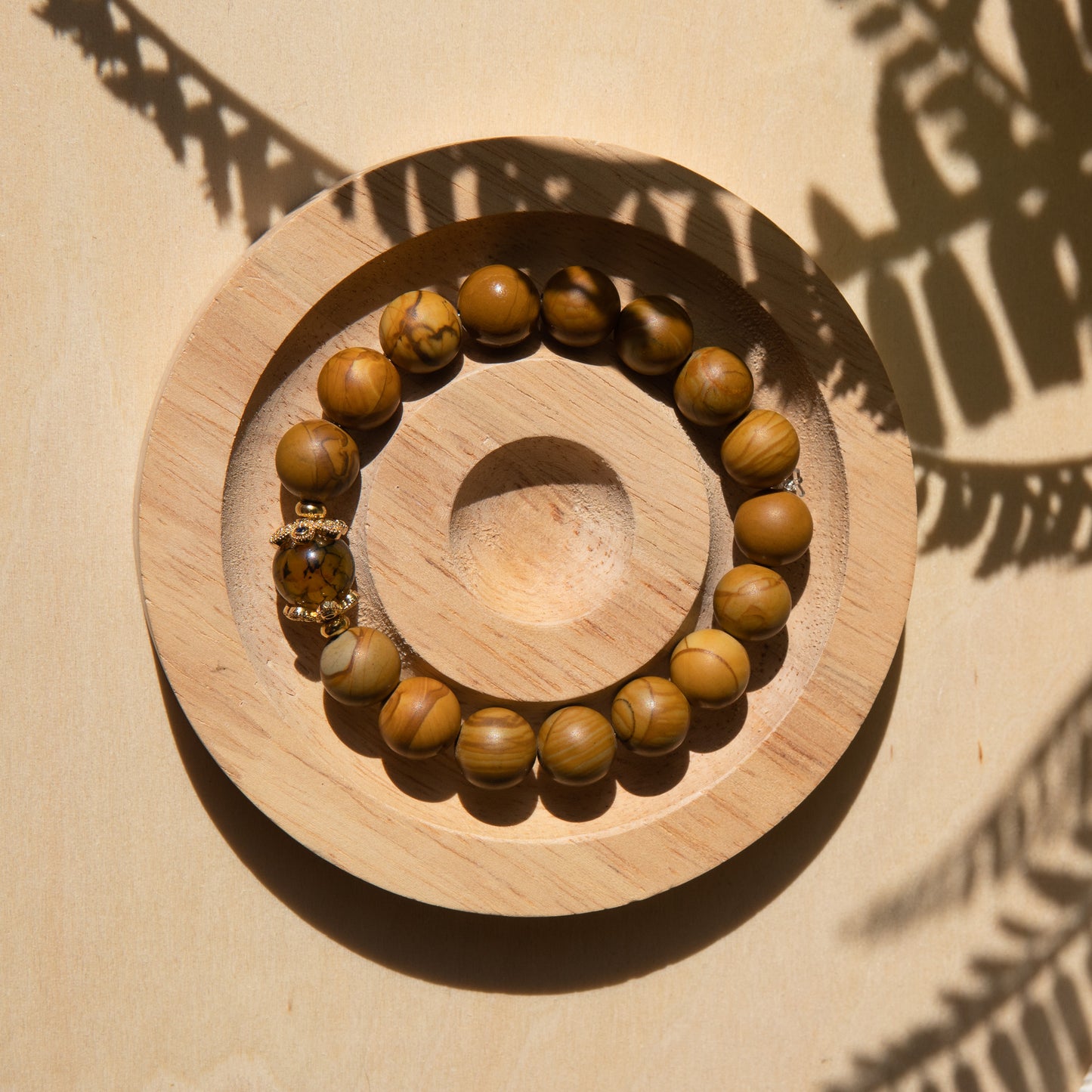A lacewood beaded bracelet with a dragon viens agate crystal, displayed on a wooden coaster with a shell in the background.