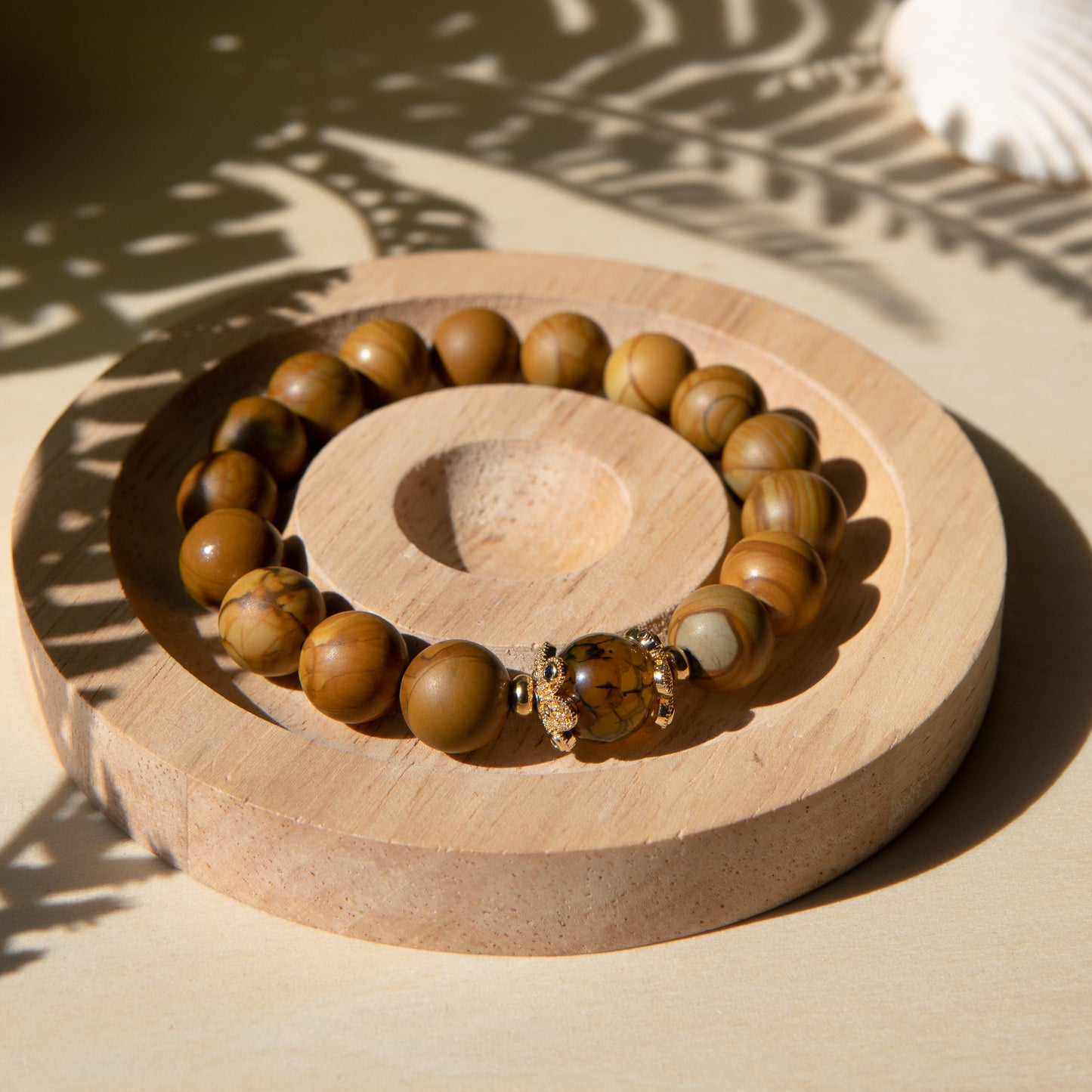 A lacewood beaded bracelet with a dragon viens agate crystal, displayed on a wooden coaster with a shell in the background.