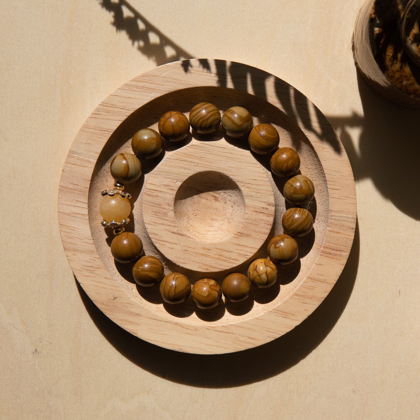 A lacewood beaded bracelet with a honey jade crystal, displayed on a wooden coaster with a shell in the background.