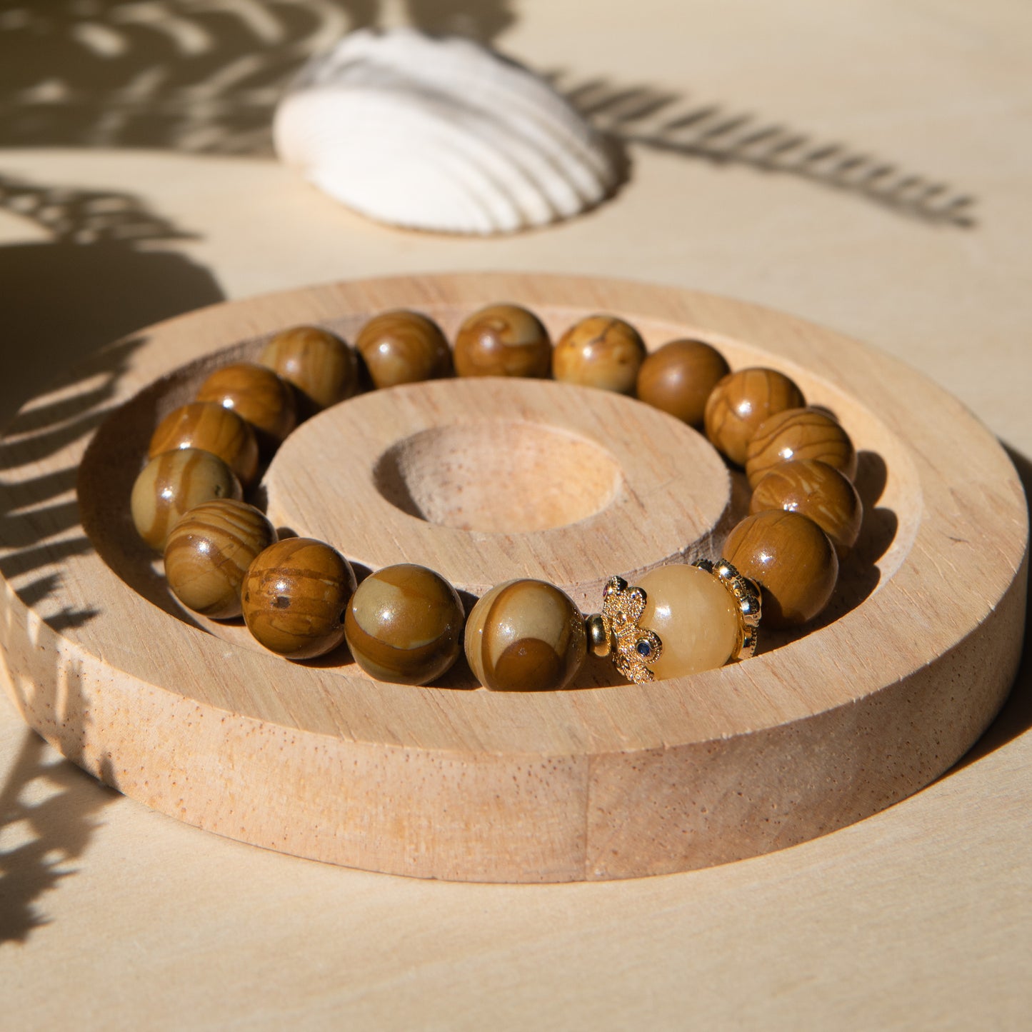 A lacewood beaded bracelet with a honey jade crystal, displayed on a wooden coaster with a shell in the background.