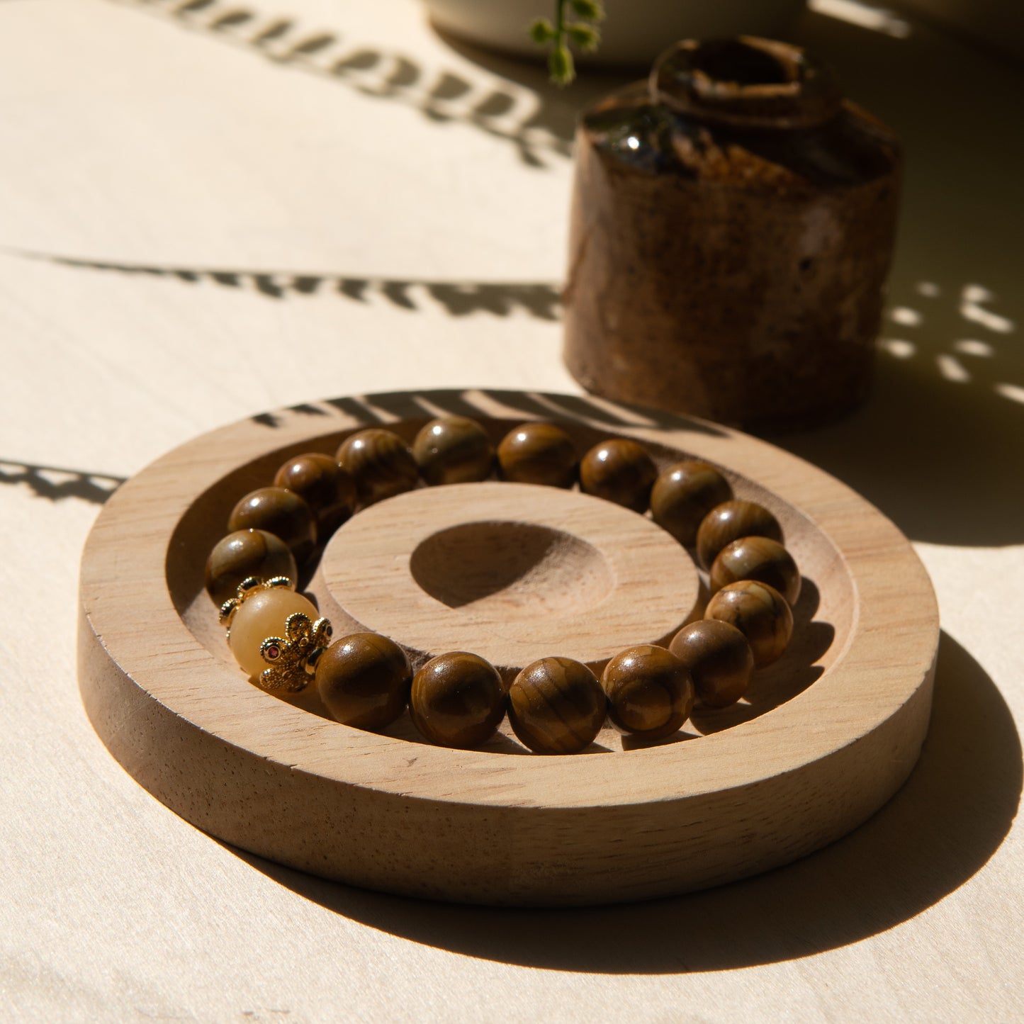 A lacewood beaded bracelet with a honey jade crystal, displayed on a wooden coaster with a shell in the background.