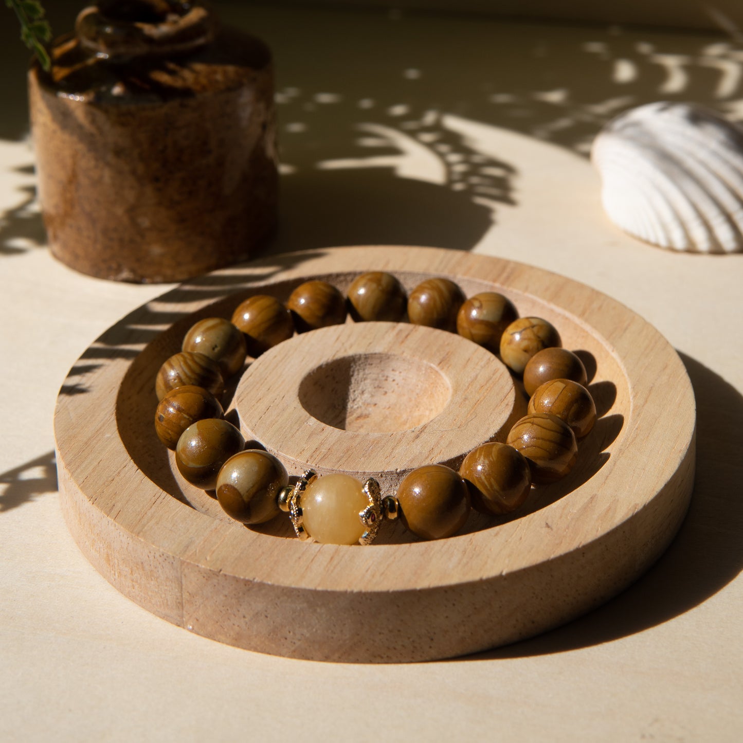 A lacewood beaded bracelet with a honey jade crystal, displayed on a wooden coaster with a shell in the background.