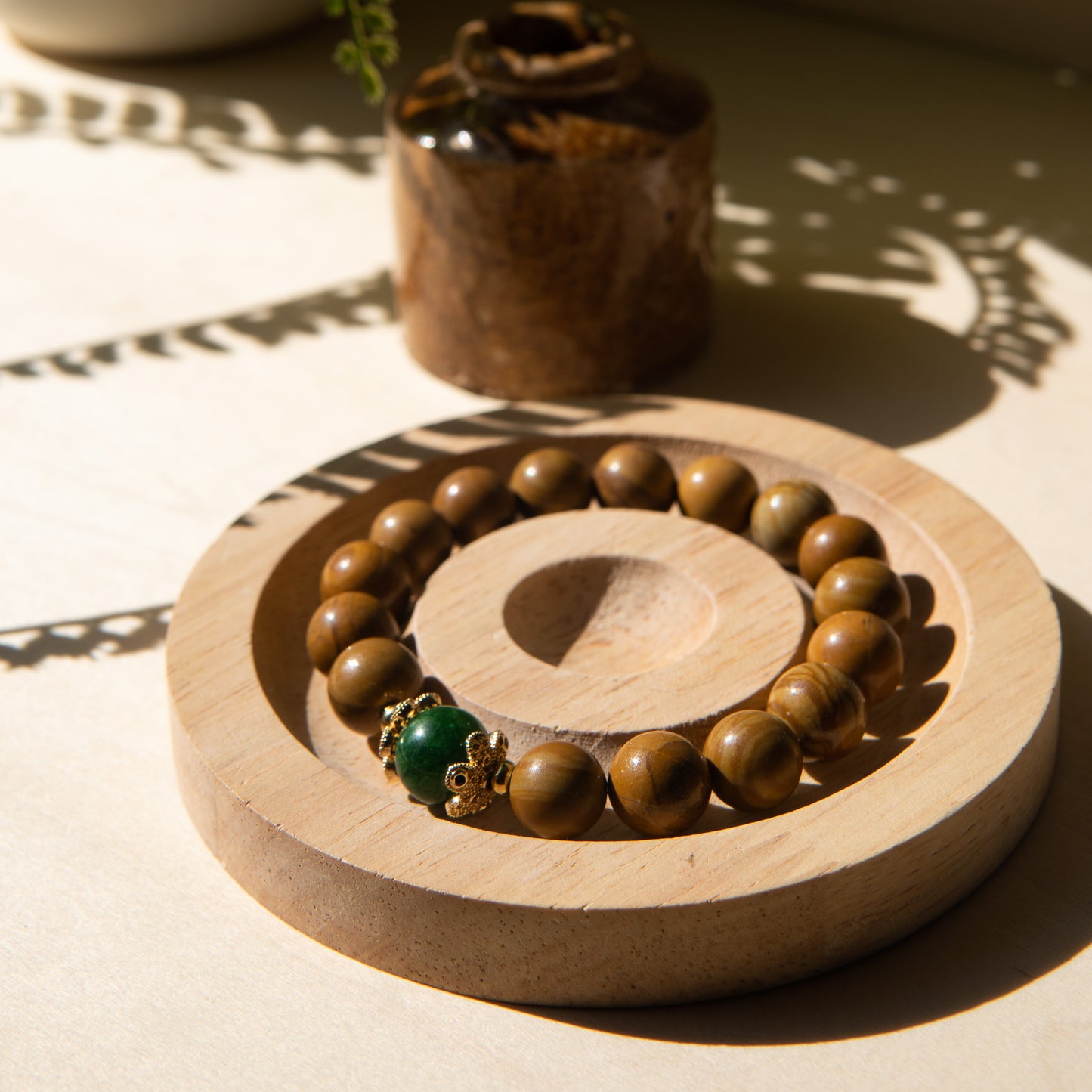 A lacewood beaded bracelet with a Malayian jade crystal, displayed on a wooden coaster with a shell in the background.