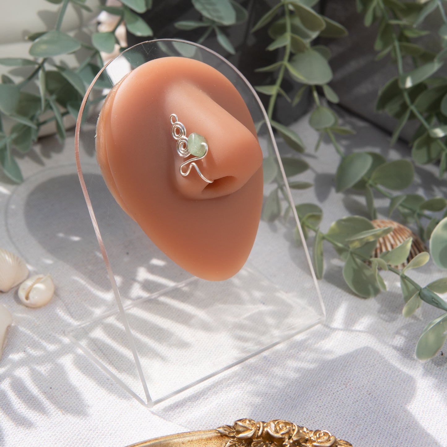 A silver-toned faux nose ring adorns the model's nose in a circular wire design that spirals up and gradually decreases in size. A crystal gemstone is woven into the design and rests at the bottom.