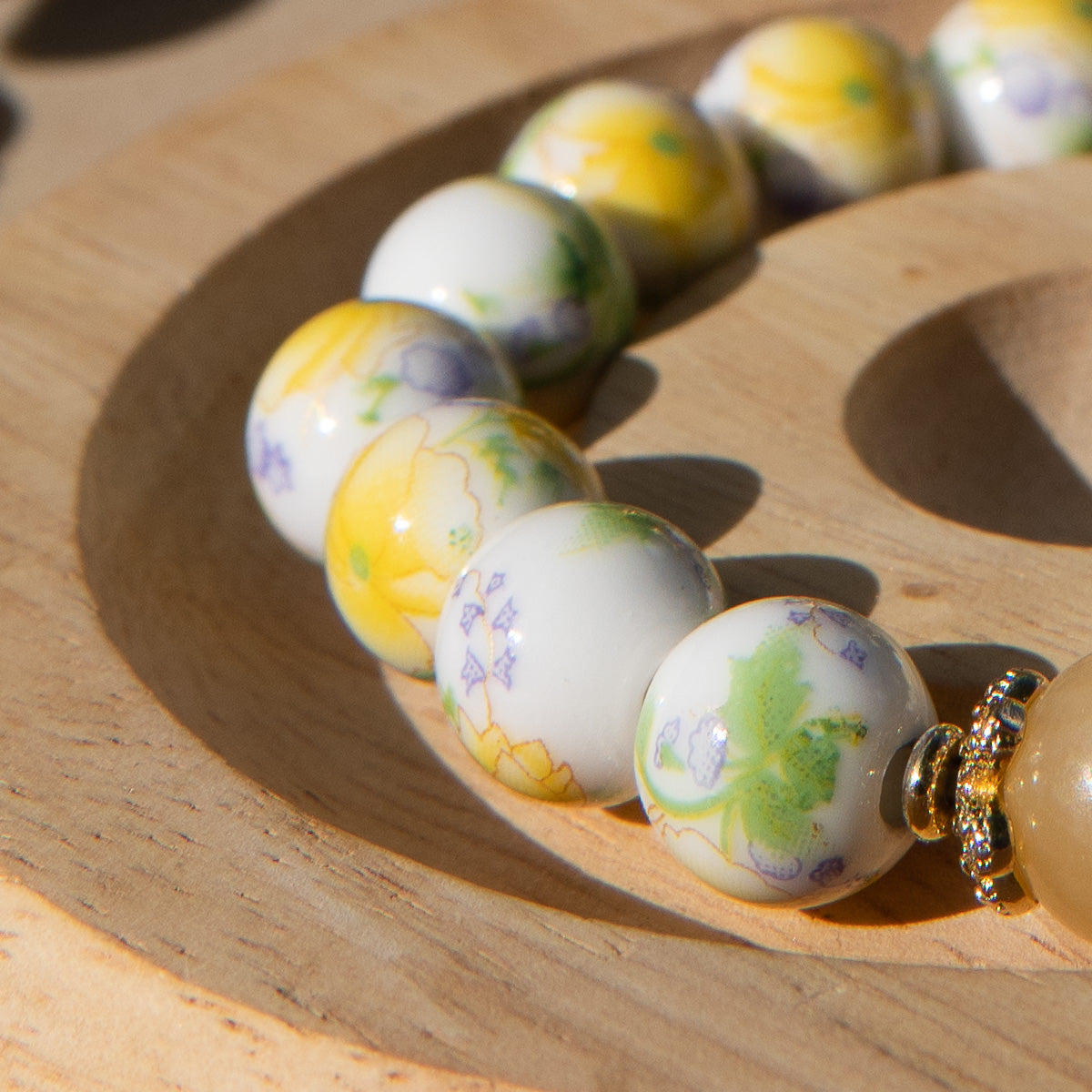 Yellow porcelain beaded bracelet with floral designs on a wooden surface
