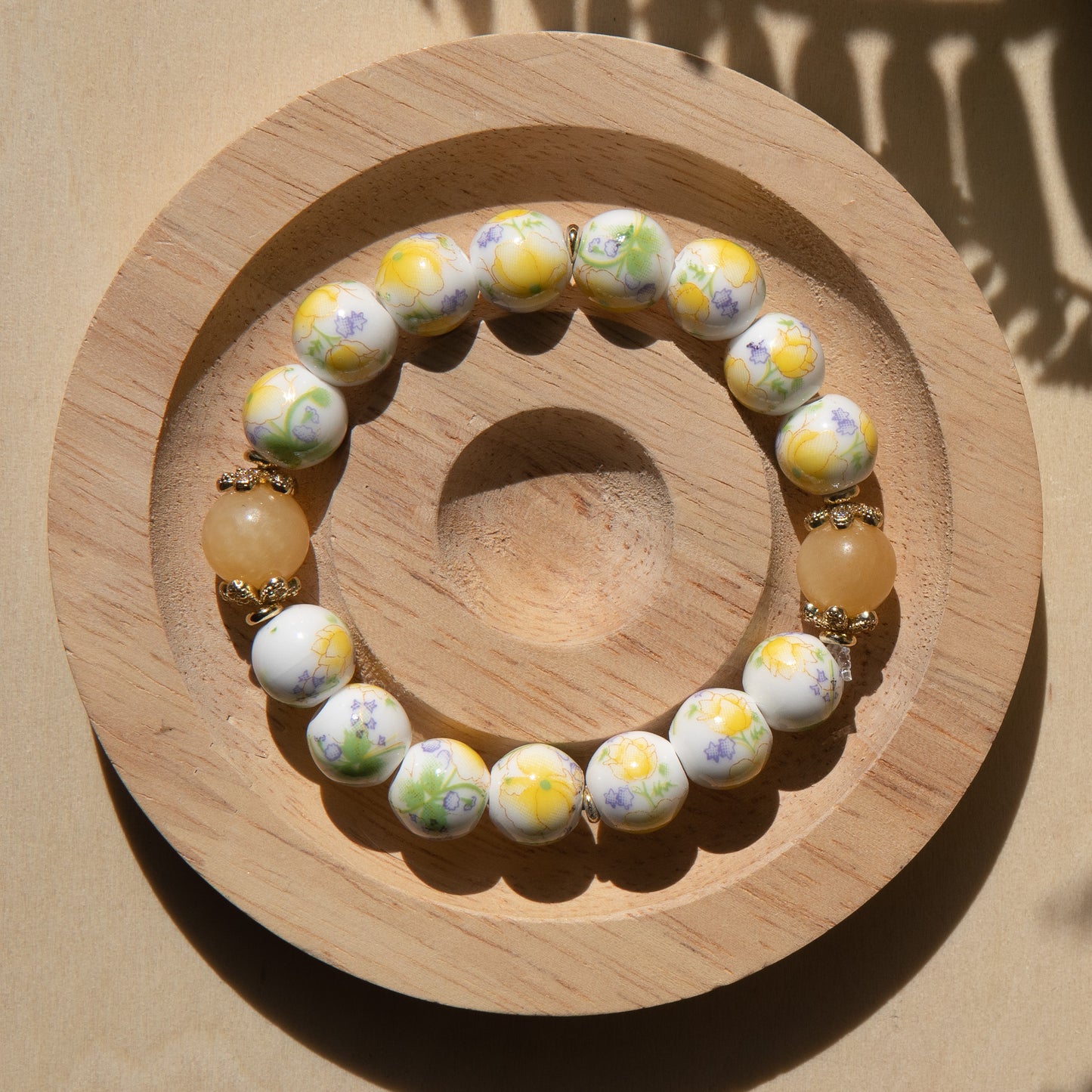 Yellow porcelain beaded bracelet embellished with honey jade crystal on a wooden tray with a shell in the background.