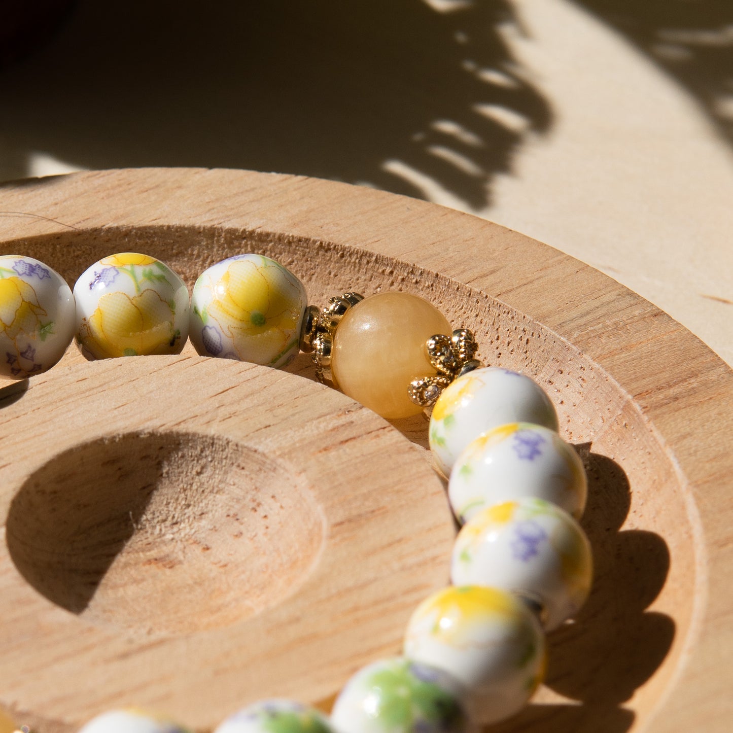 Yellow porcelain beaded bracelet embellished with honey jade crystal on a wooden tray with a shell in the background.
