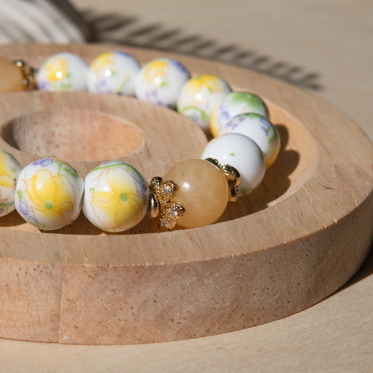 Yellow porcelain beaded bracelet embellished with honey jade crystal on a wooden tray with a shell in the background.
