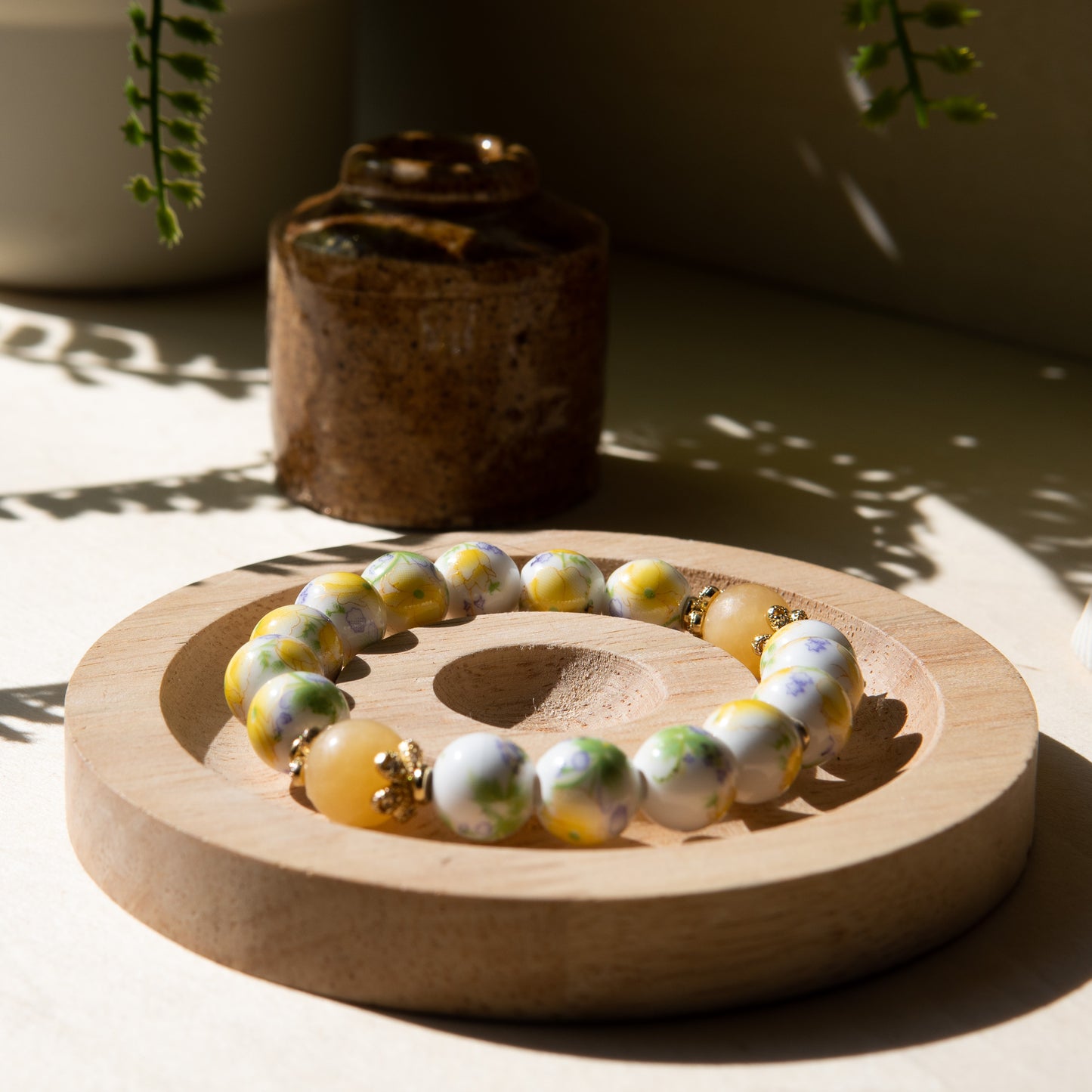 Yellow porcelain beaded bracelet embellished with honey jade crystal on a wooden tray with a shell in the background.
