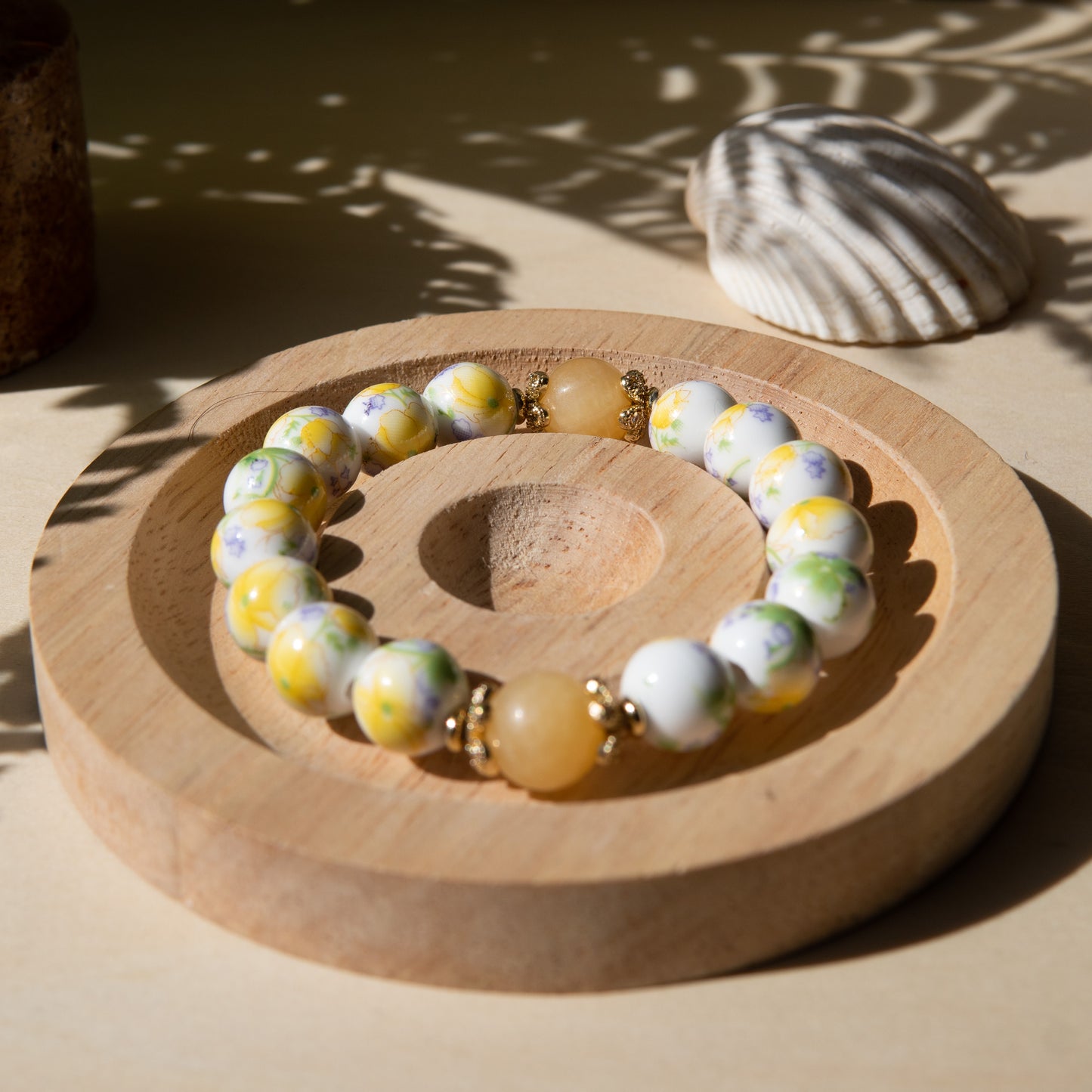 Yellow porcelain beaded bracelet embellished with honey jade crystal on a wooden tray with a shell in the background.