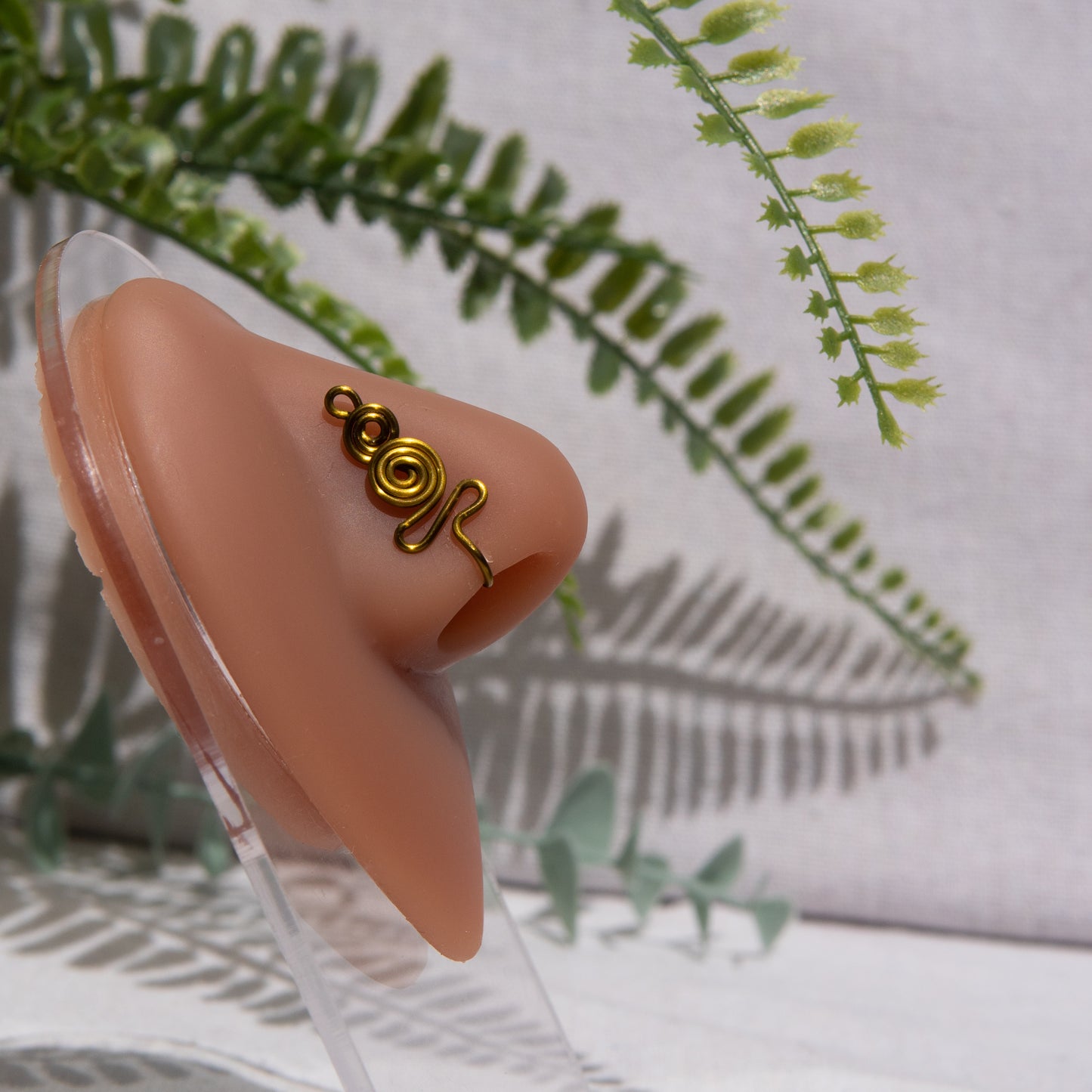 A bronze-toned nose cuff adorns the model's nose in a circular wire design that spirals up and gradually decreases in size.