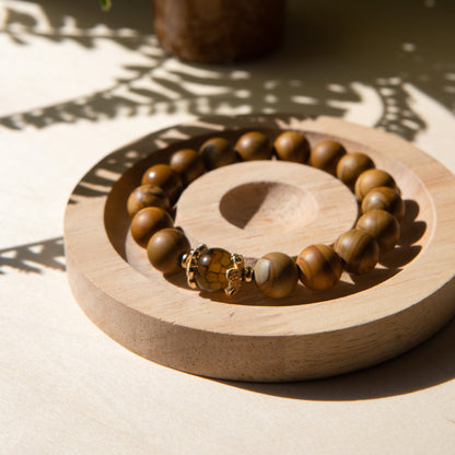A lacewood beaded bracelet with a dragon viens agate crystal, displayed on a wooden coaster with a shell in the background.