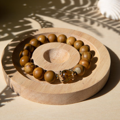 A lacewood beaded bracelet with a dragon viens agate crystal, displayed on a wooden coaster with a shell in the background.