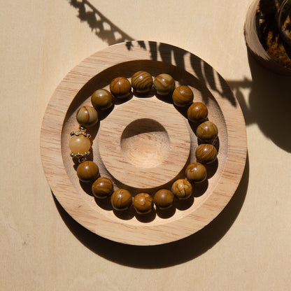 A lacewood beaded bracelet with a honey jade crystal, displayed on a wooden coaster with a shell in the background.