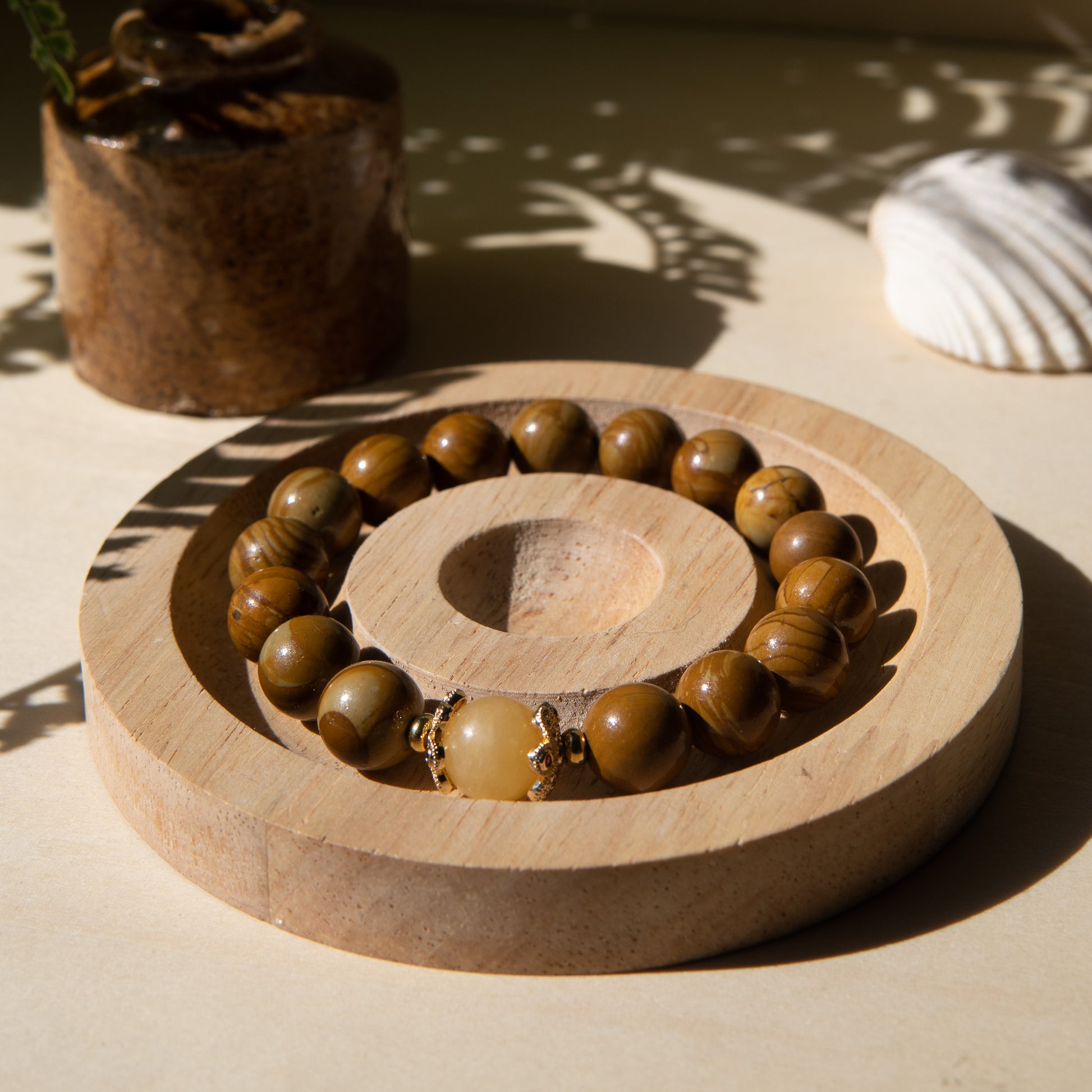 A lacewood beaded bracelet with a honey jade crystal, displayed on a wooden coaster with a shell in the background.