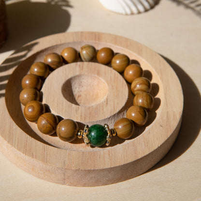 A lacewood beaded bracelet with a Malayian jade crystal, displayed on a wooden coaster with a shell in the background.
