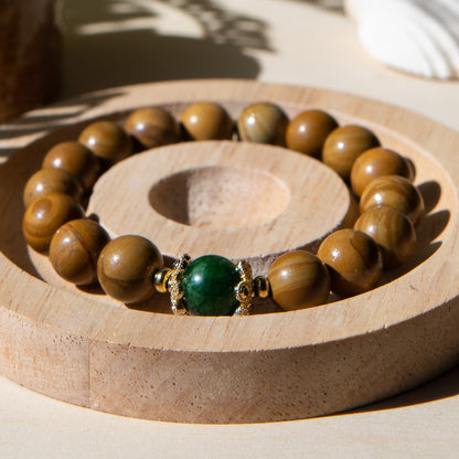 A lacewood beaded bracelet with a Malayian jade crystal, displayed on a wooden coaster with a shell in the background.