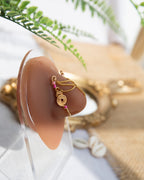 A gold-toned faux chain bridge nose piercing cuffs both of the model's nostrils. Two dainty 18K gold-plated curb chains rest across the bridge of the nose attached to the top and middle of each cuff, forming a criss-cross shape. Three pink seed beads were interweaved into the design of each nose cuff.