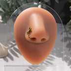 A bronze-toned nose piercing cuffs the model's nostril. The wire design forms an Egyptian Ankh symbol. 