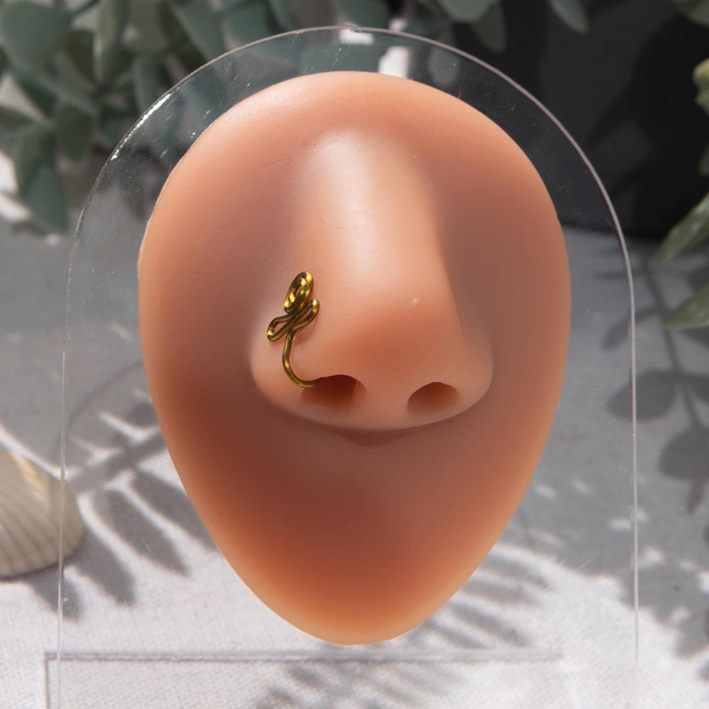 A bronze-toned nose piercing cuffs the model's nostril. The wire design forms an Egyptian Ankh symbol. 