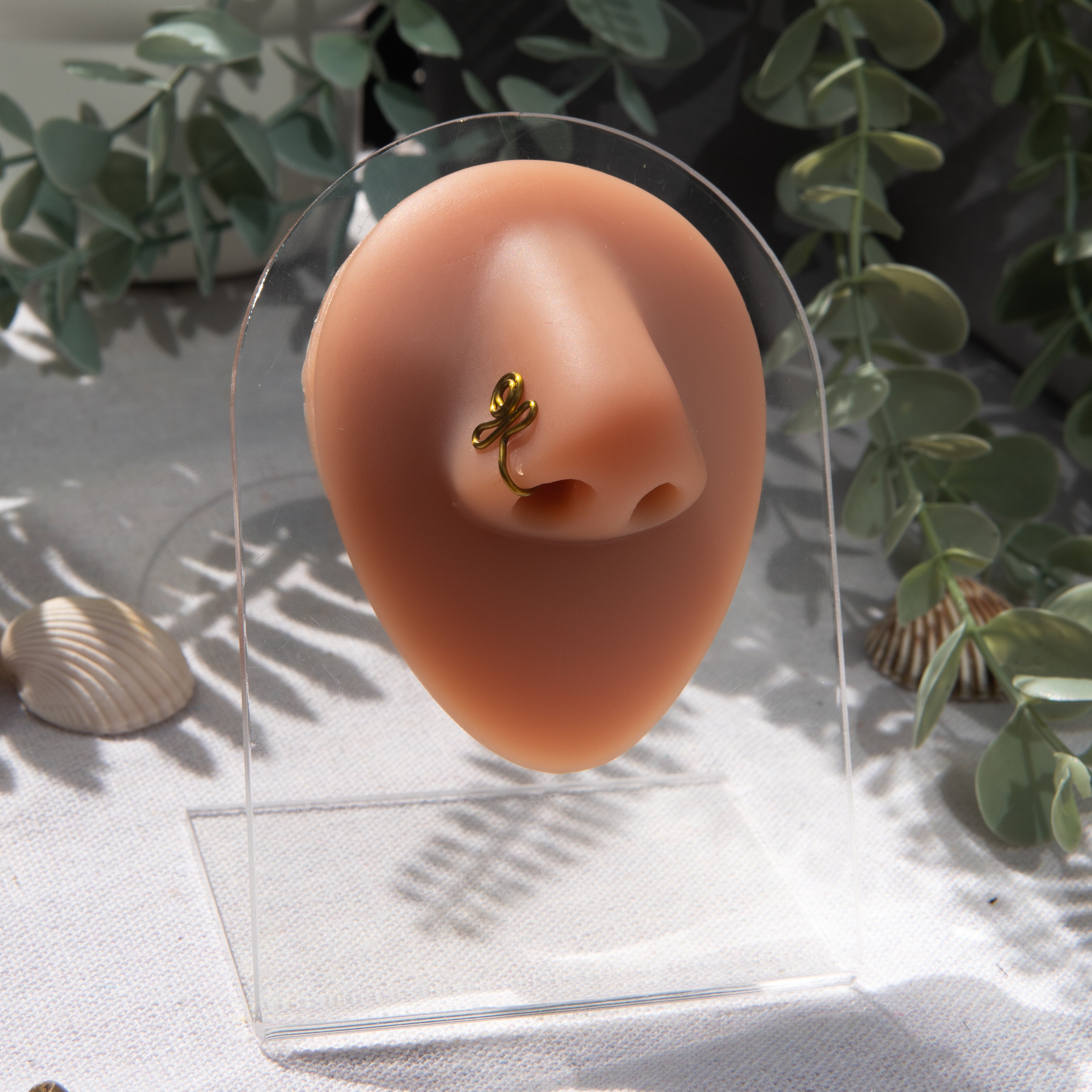 A bronze-toned nose piercing cuffs the model's nostril. The wire design forms an Egyptian Ankh symbol. 