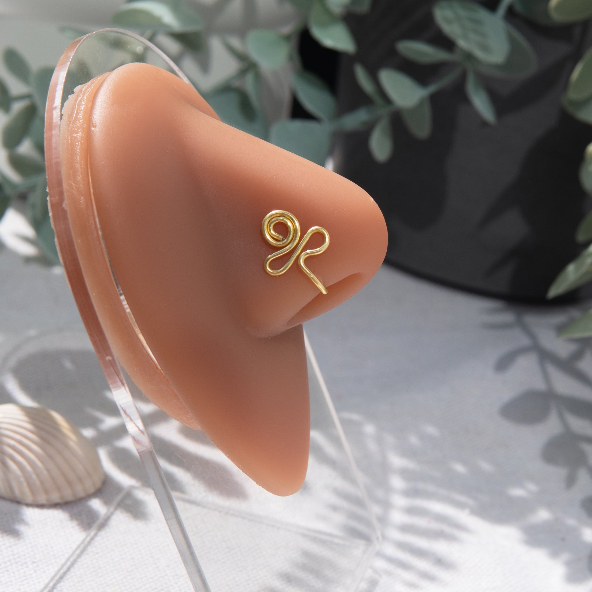 A light gold-toned nose piercing cuffs the model's nostril. The wire design forms an Egyptian Ankh symbol. 