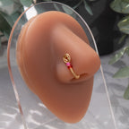 A gold-toned nose cuff rests on the model's nostril. The wire design forms a circular shape, with two pink seed beads resting below the circle. 