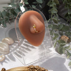 A light gold-toned fake nose ring cuffs the model's nostril. The wire design forms a circular shape. Two seed beads (yellow and lilac) rest below the circle.