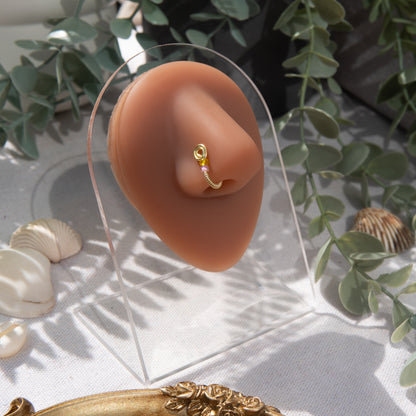 A light gold-toned fake nose ring cuffs the model's nostril. The wire design forms a circular shape. Two seed beads (yellow and lilac) rest below the circle.