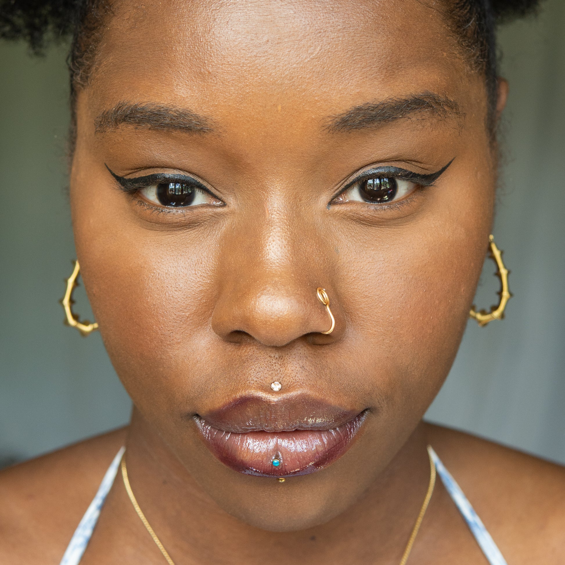 A gold-toned faux nose ring cuffs the model's nose. The wire design is shaped into a circular form.