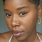 A gold-toned faux nose ring cuffs the model's nose. The wire design is shaped into a circular form.
