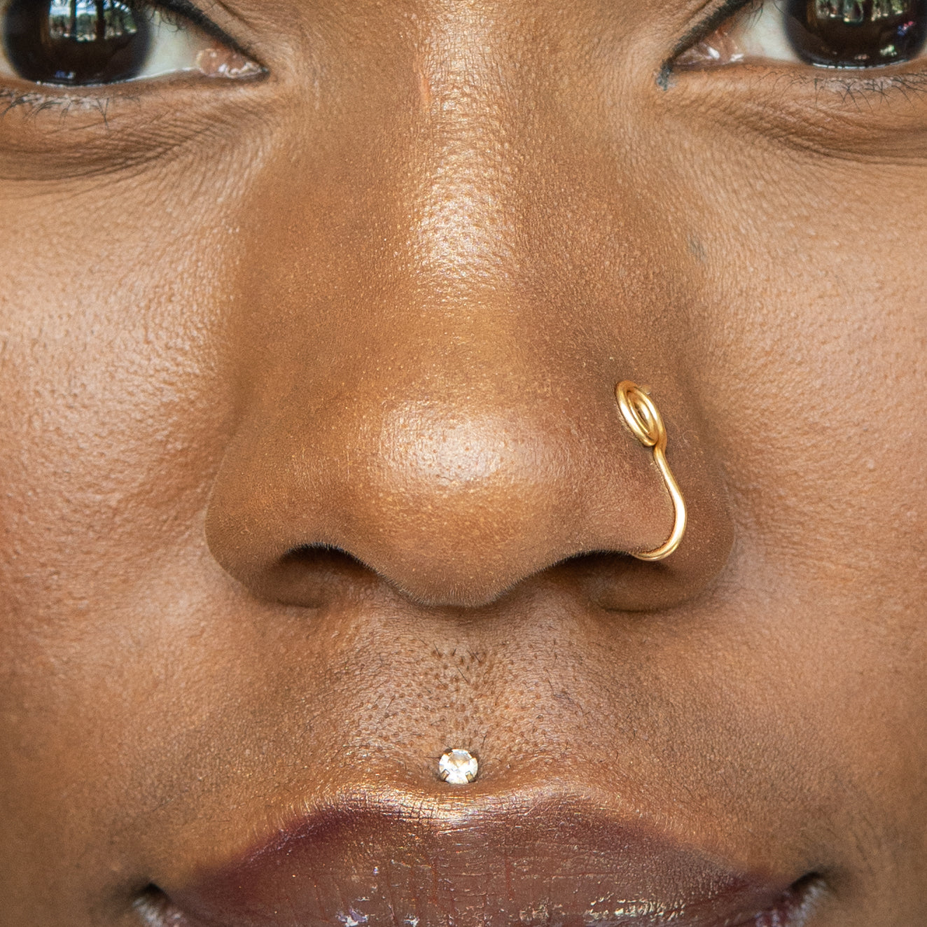 A gold-toned faux nose ring cuffs the model's nose. The wire design is shaped into a circular form.