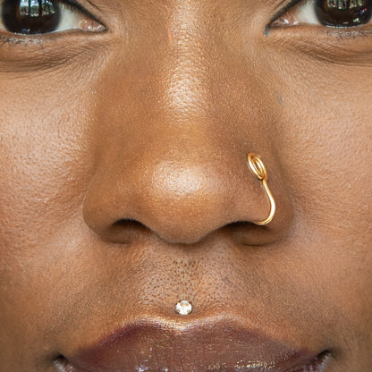 A gold-toned faux nose ring cuffs the model's nose. The wire design is shaped into a circular form.