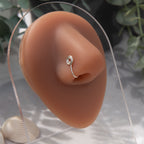 A silver-toned faux nose ring cuffs the model's nose. The wire design is shaped into a circular form.