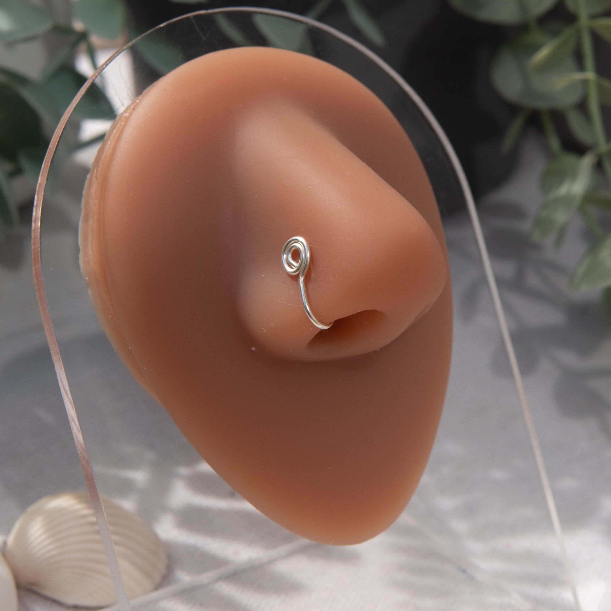 A silver-toned faux nose ring cuffs the model's nose. The wire design is shaped into a circular form.