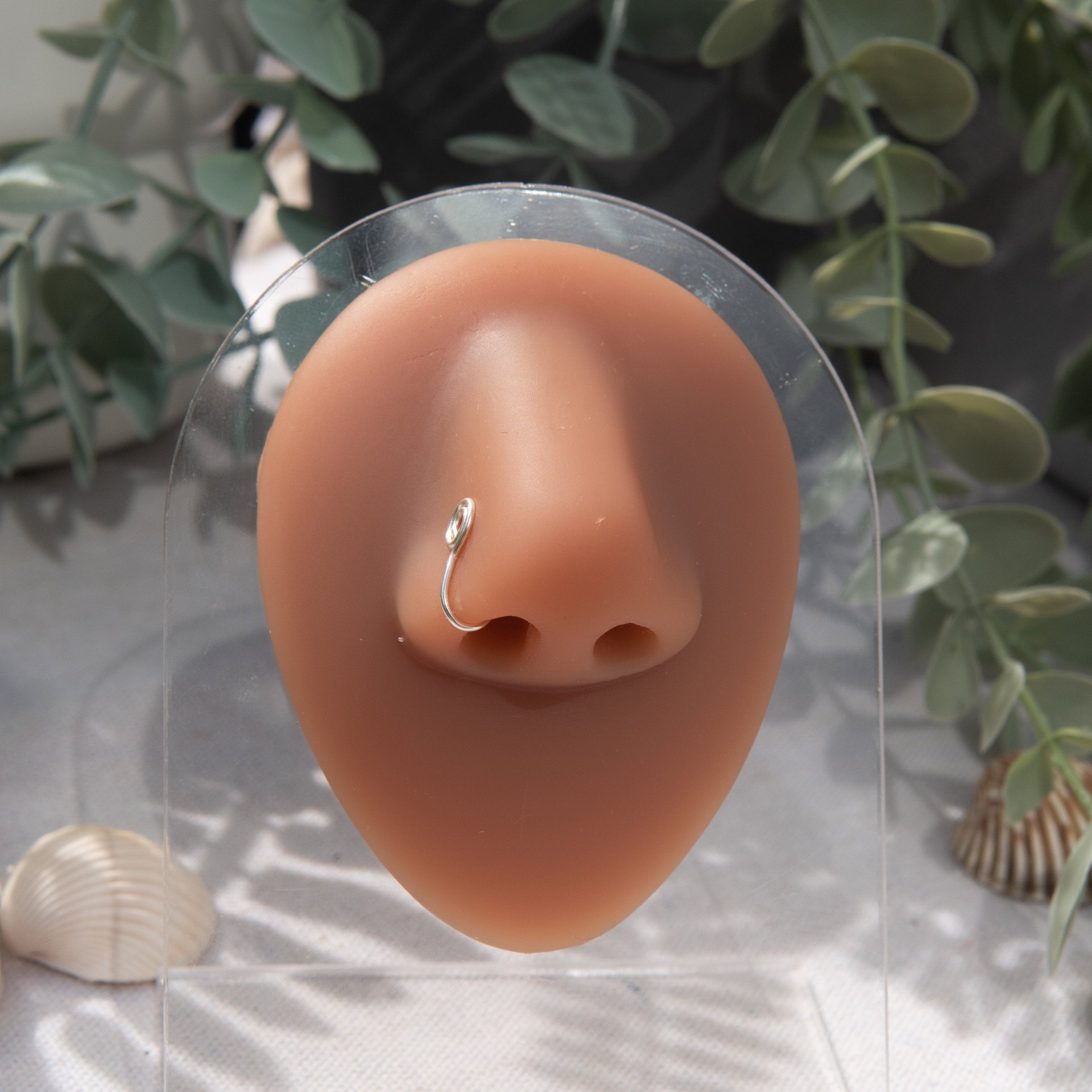 A silver-toned faux nose ring cuffs the model's nose. The wire design is shaped into a circular form.