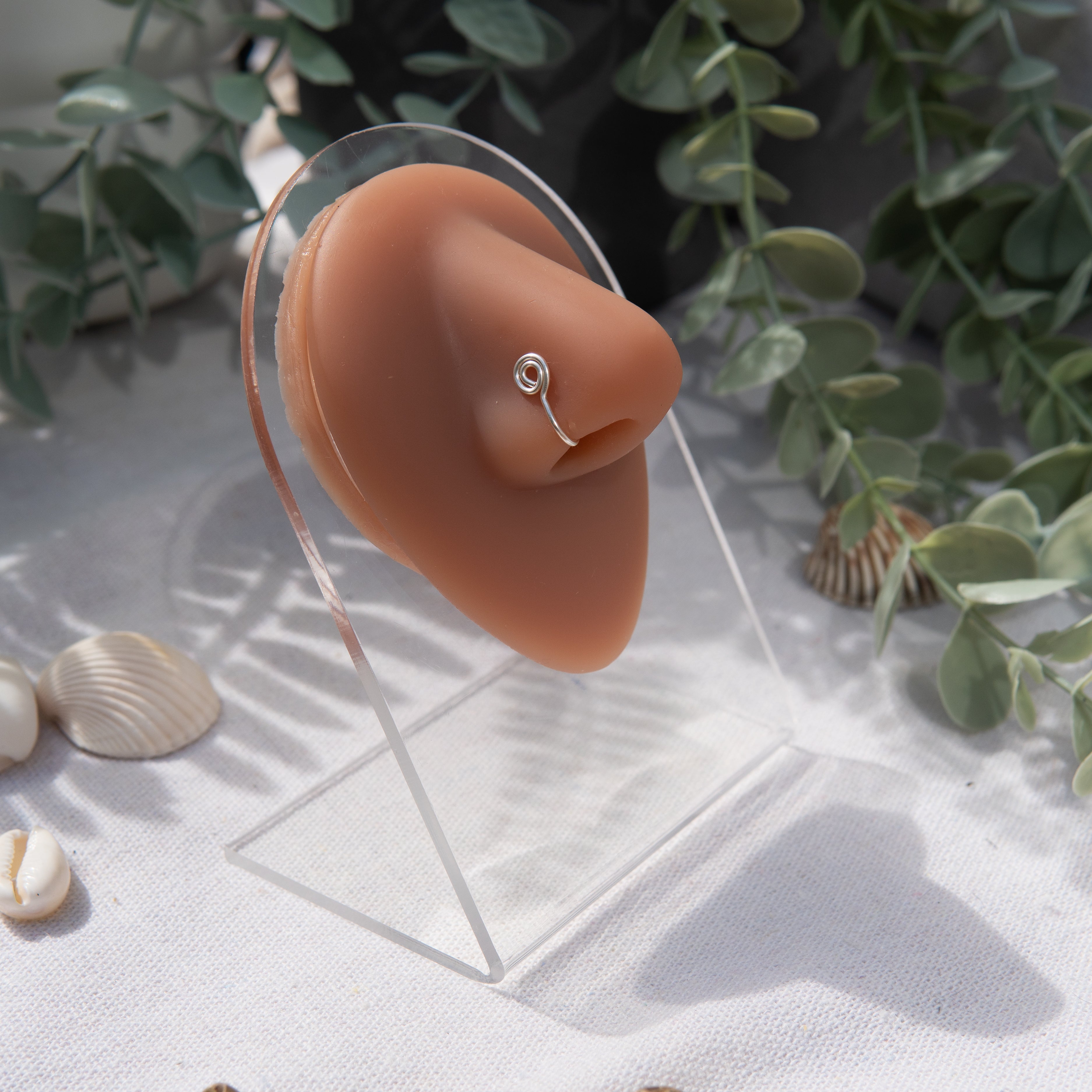 A silver-toned faux nose ring cuffs the model's nose. The wire design is shaped into a circular form.