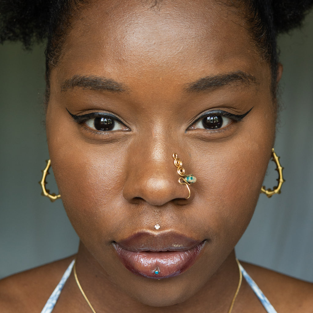 A gold-toned faux nose ring adorns the model's nose in a circular wire design that spirals up and gradually decreases in size. A crystal amazonite gemstone is woven into the design and rests at the bottom.