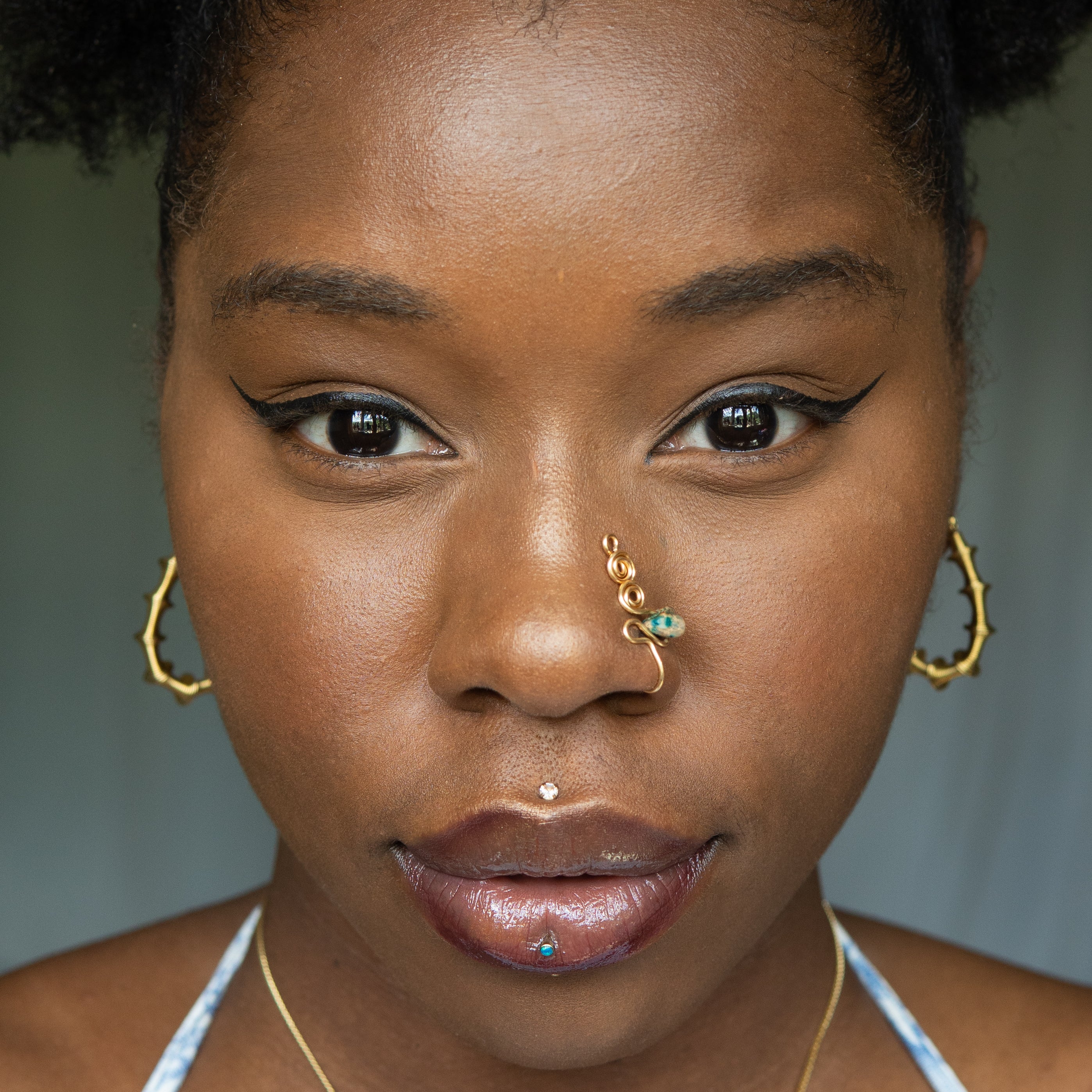 A gold-toned faux nose ring adorns the model's nose in a circular wire design that spirals up and gradually decreases in size. A crystal amazonite gemstone is woven into the design and rests at the bottom.