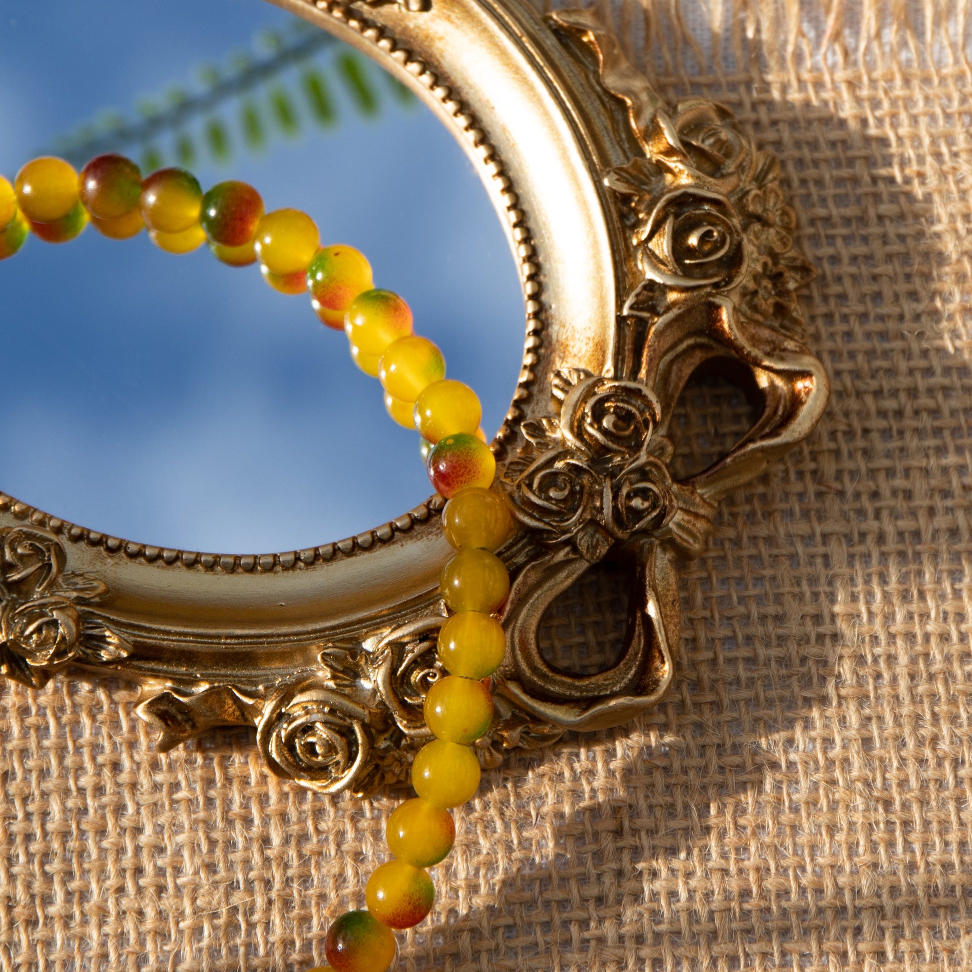 An elastic choker necklace adorned with ombré spray-painted glass beads. The beads' primary colour is golden-yellow, with additional shades of burnt orange and green. Two gold-plated space beads reside in the middle of the choker.