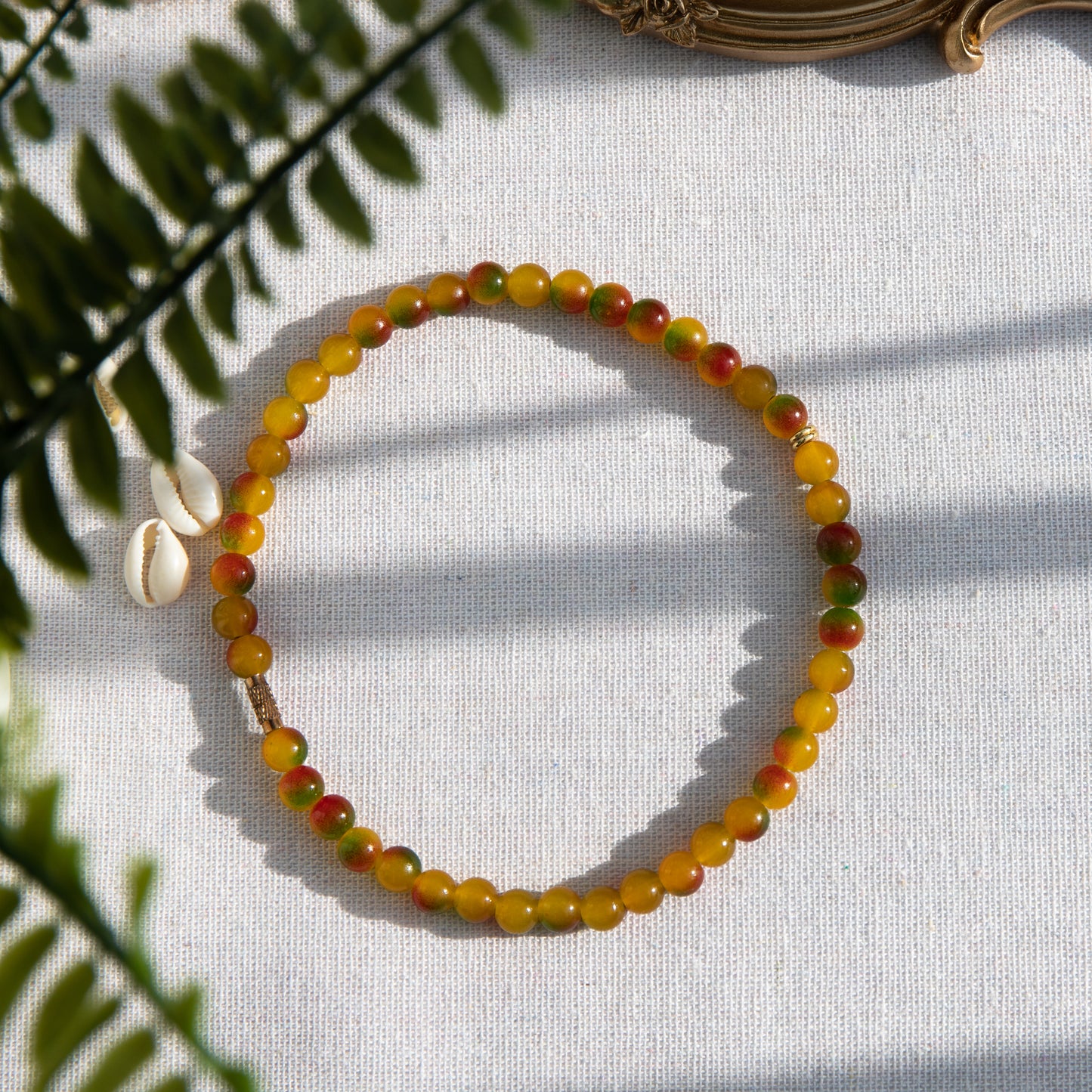 An elastic choker necklace adorned with ombré spray-painted glass beads. The beads' primary colour is golden-yellow, with additional shades of burnt orange and green. Two gold-plated space beads reside in the middle of the choker.