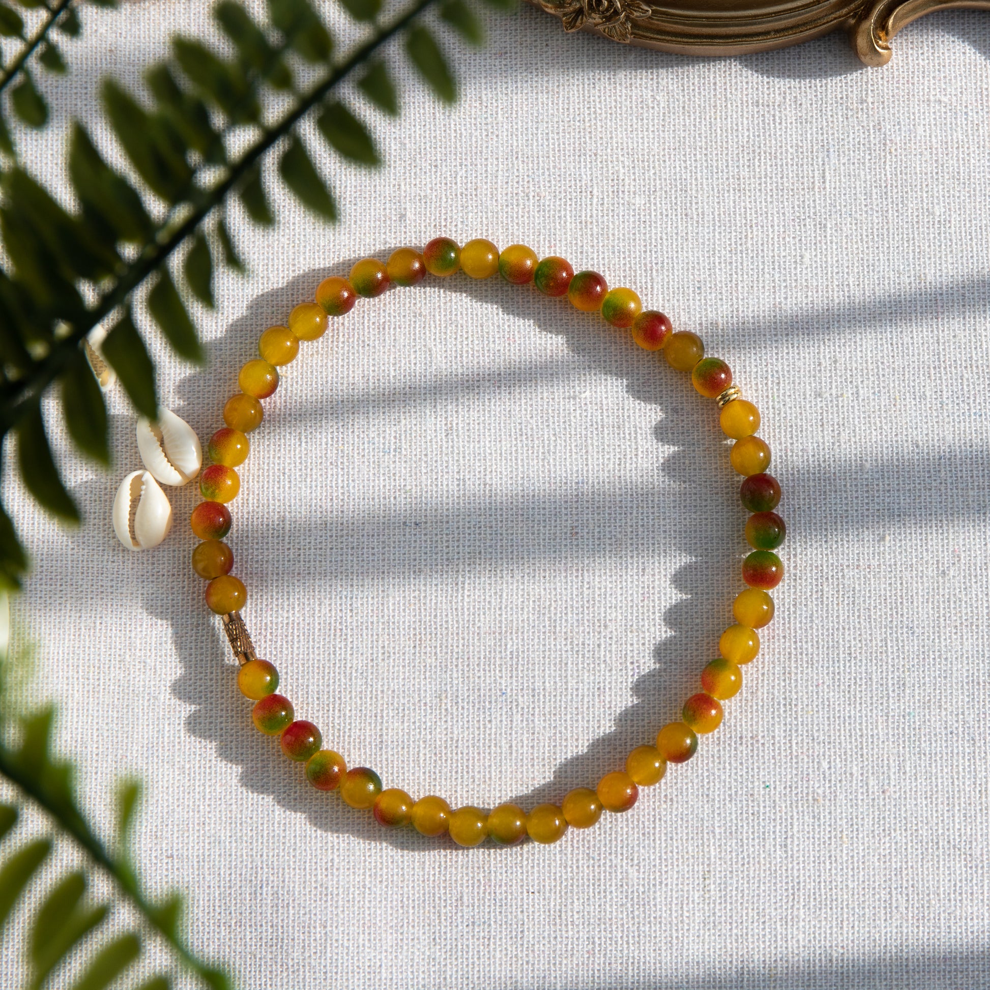 An elastic choker necklace adorned with ombré spray-painted glass beads. The beads' primary colour is golden-yellow, with additional shades of burnt orange and green. Two gold-plated space beads reside in the middle of the choker.