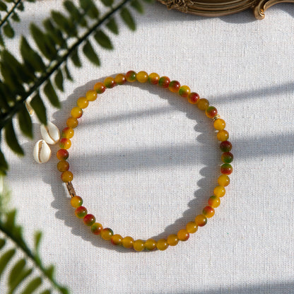 An elastic choker necklace adorned with ombré spray-painted glass beads. The beads' primary colour is golden-yellow, with additional shades of burnt orange and green. Two gold-plated space beads reside in the middle of the choker.