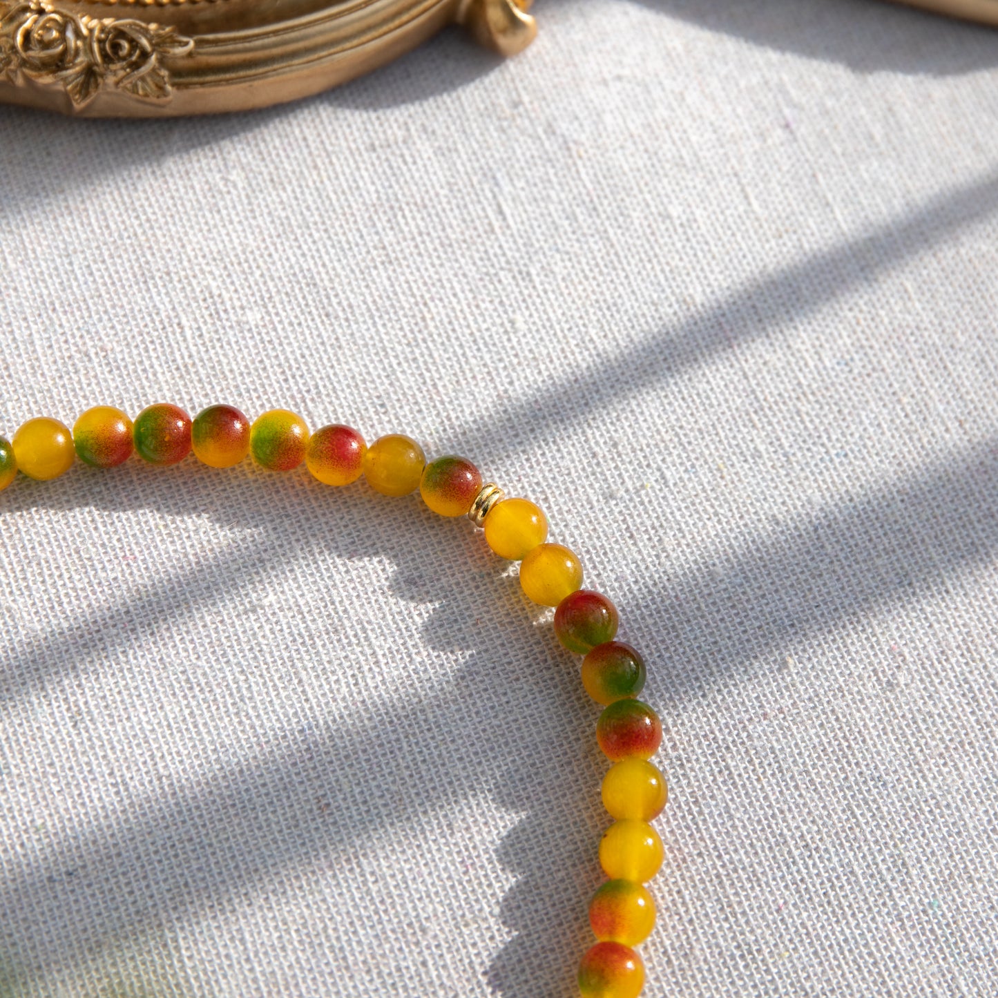 An elastic choker necklace adorned with ombré spray-painted glass beads. The beads' primary colour is golden-yellow, with additional shades of burnt orange and green. Two gold-plated space beads reside in the middle of the choker.