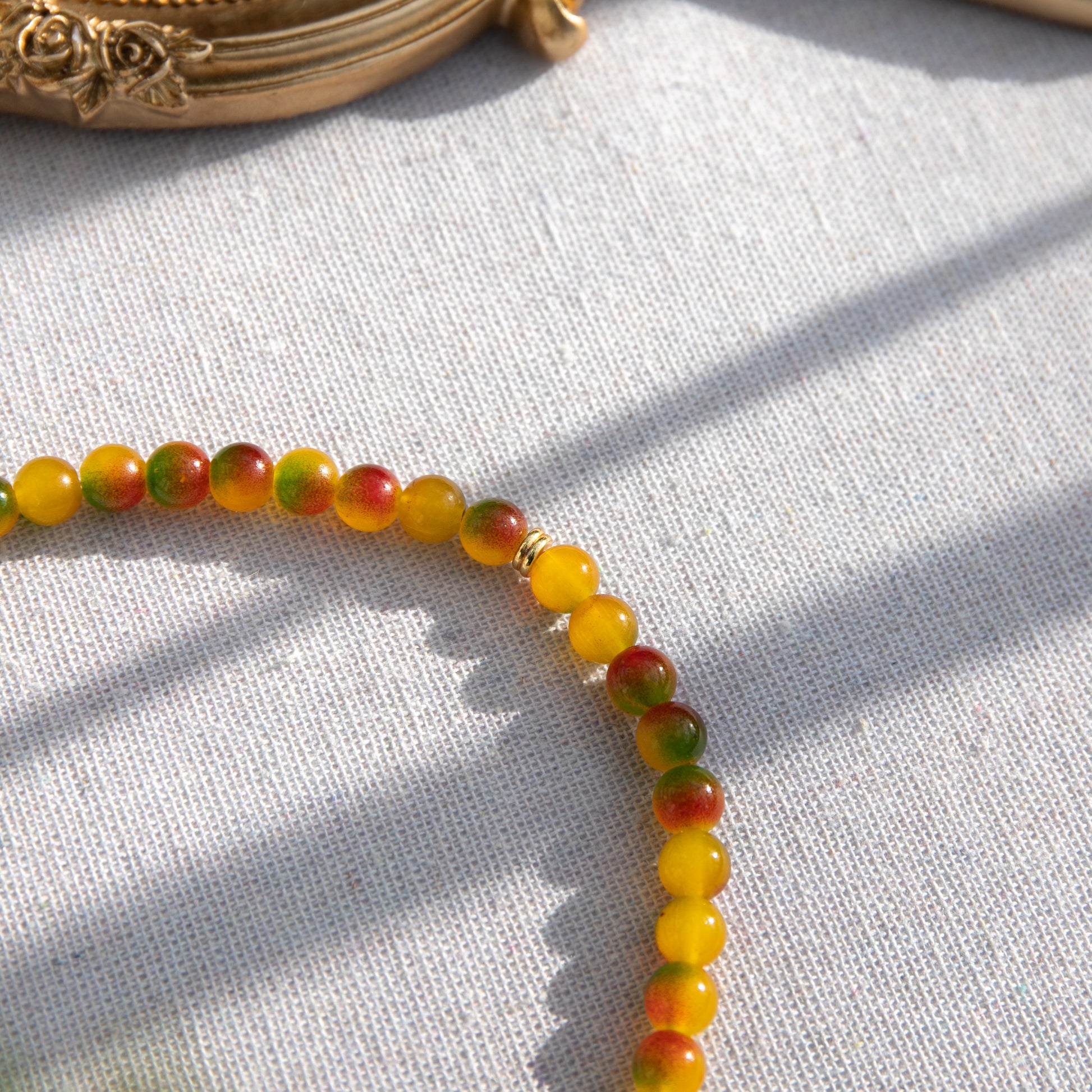 An elastic choker necklace adorned with ombré spray-painted glass beads. The beads' primary colour is golden-yellow, with additional shades of burnt orange and green. Two gold-plated space beads reside in the middle of the choker.