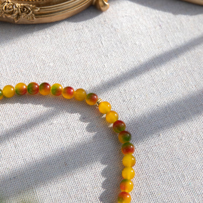 An elastic choker necklace adorned with ombré spray-painted glass beads. The beads' primary colour is golden-yellow, with additional shades of burnt orange and green. Two gold-plated space beads reside in the middle of the choker.