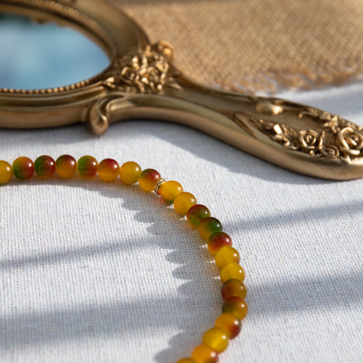 An elastic choker necklace adorned with ombré spray-painted glass beads. The beads' primary colour is golden-yellow, with additional shades of burnt orange and green. Two gold-plated space beads reside in the middle of the choker.