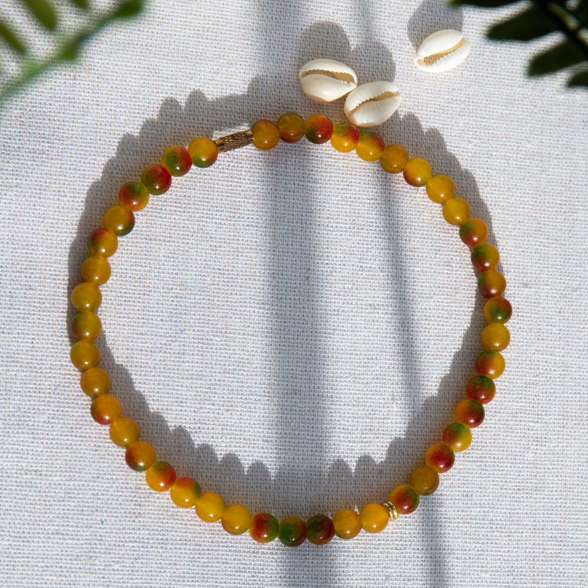 An elastic choker necklace adorned with ombré spray-painted glass beads. The beads' primary colour is golden-yellow, with additional shades of burnt orange and green. Two gold-plated space beads reside in the middle of the choker.