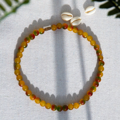 An elastic choker necklace adorned with ombré spray-painted glass beads. The beads' primary colour is golden-yellow, with additional shades of burnt orange and green. Two gold-plated space beads reside in the middle of the choker.